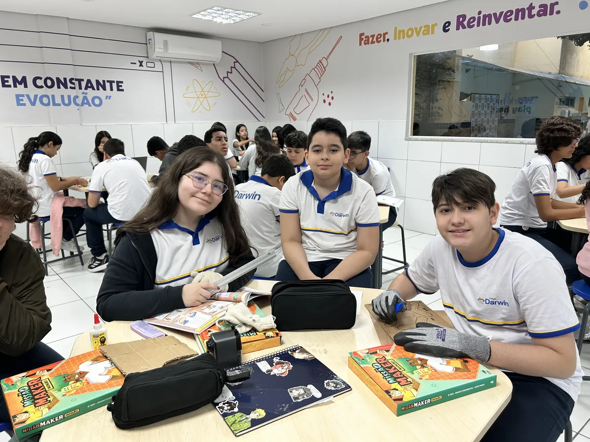 Três alunos dos Anos Finais sorrindo em torno de projeto colaborativo.