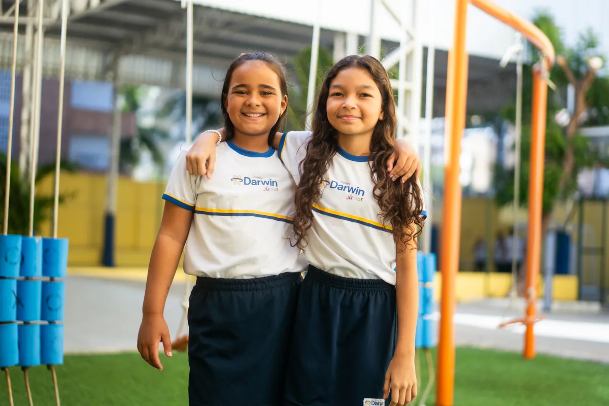 Duas alunas dos Anos Iniciais abraçadas sorrindo no pátio da escola.