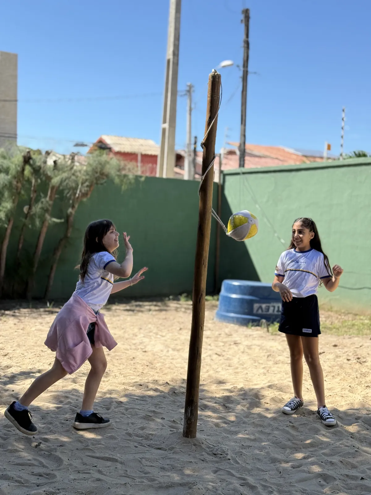 Duas meninas brincando de tetherball no parquinho de areia.