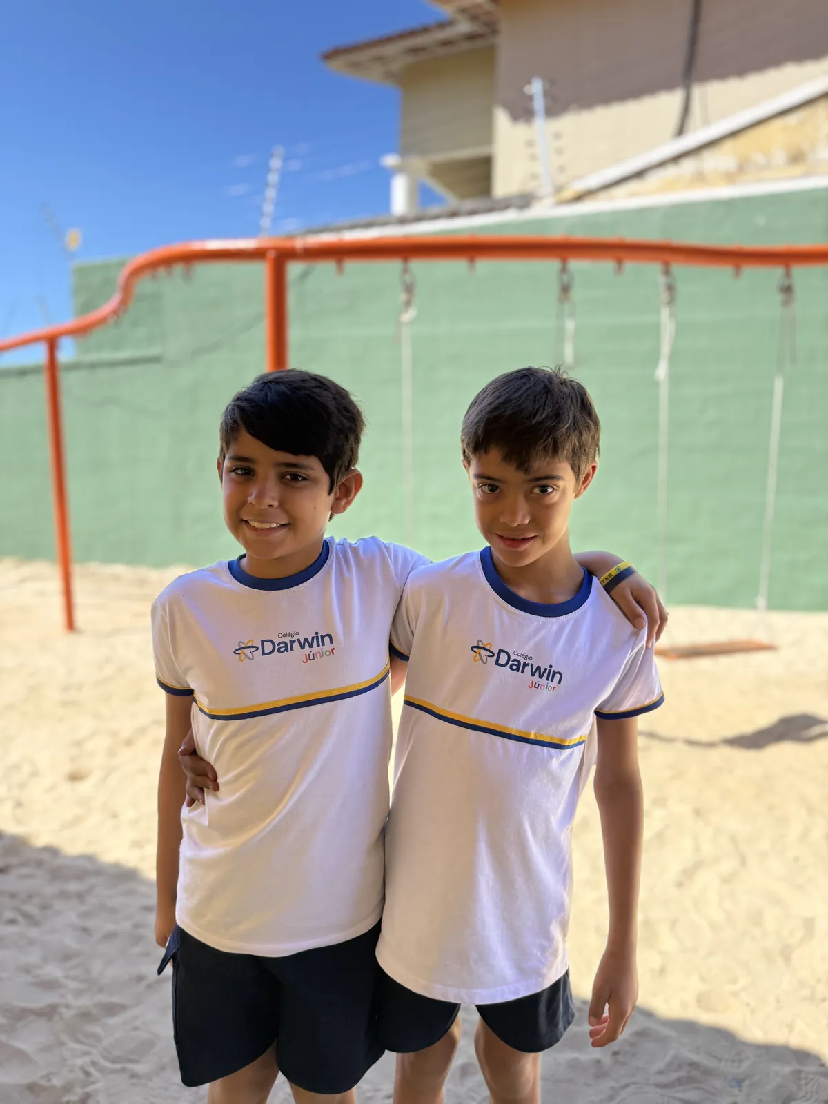 Dois meninos sorrindo em quadra esportiva de areia.