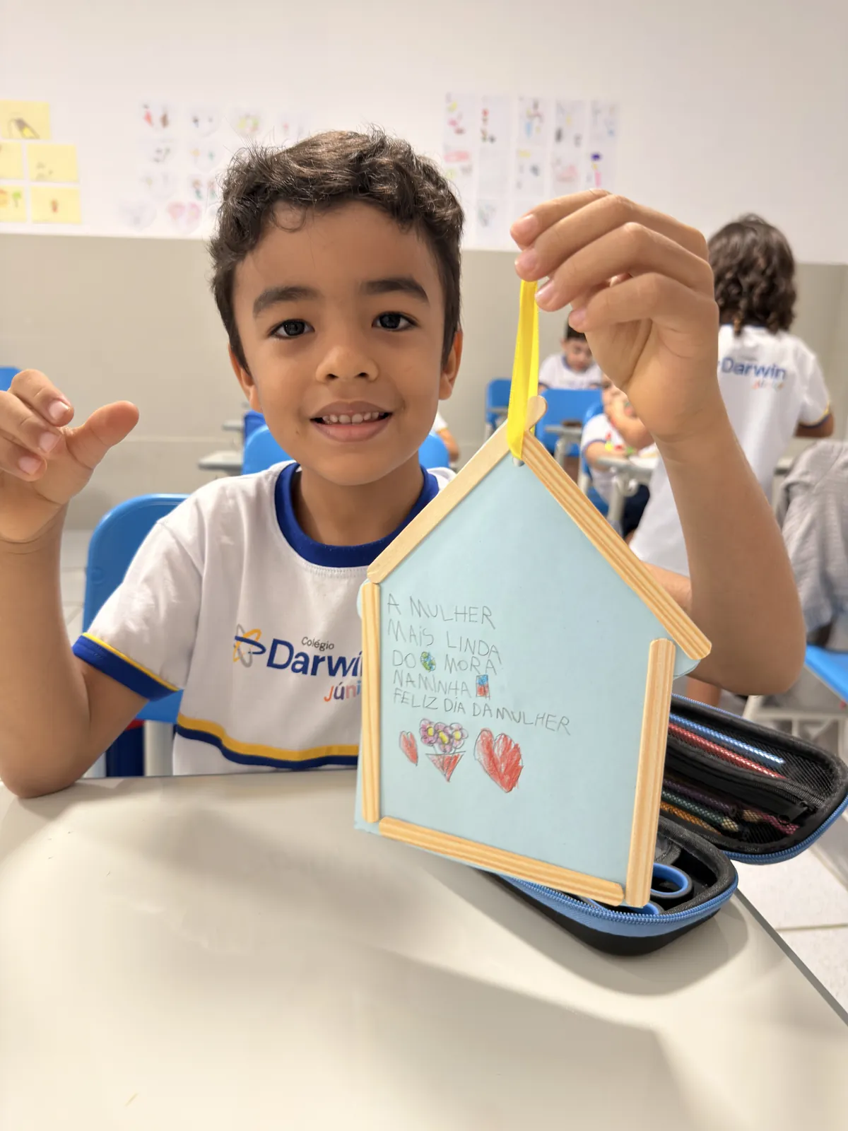 Aluno segurando casinha de papel com cartão para o Dia da Mulher.