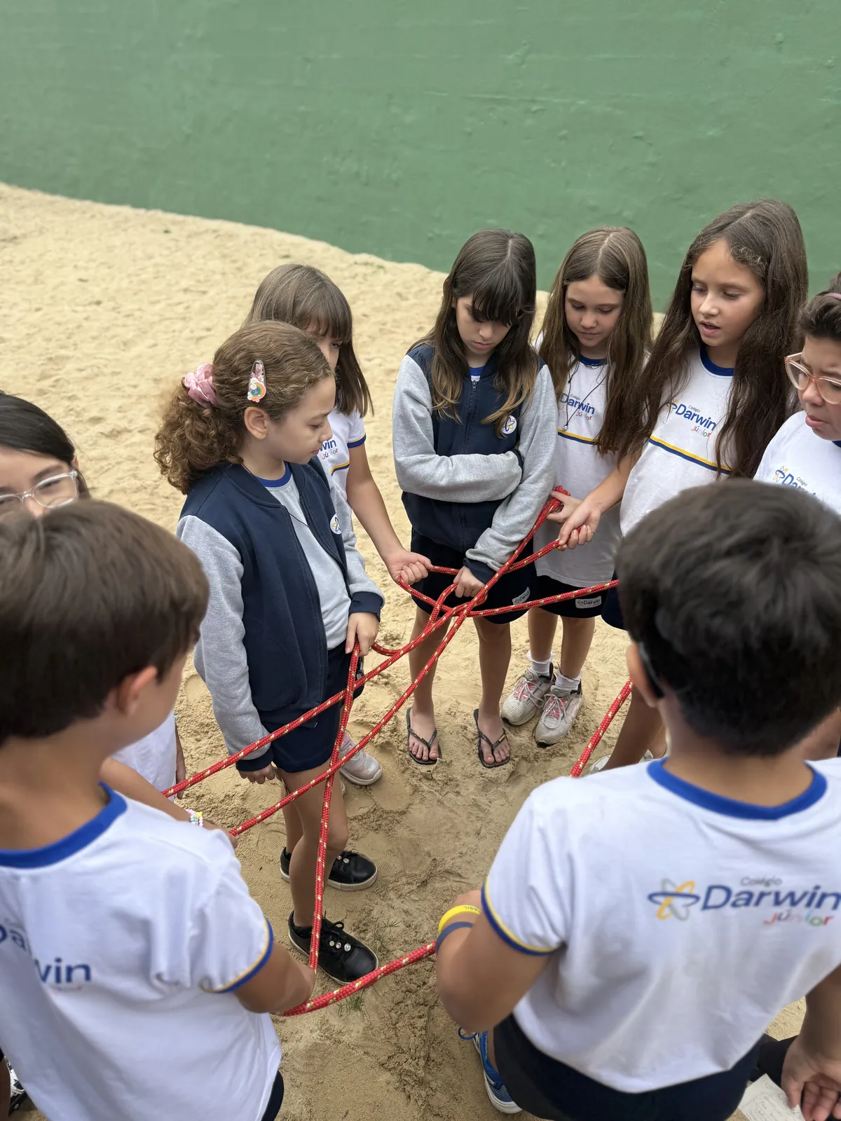 Alunos participando de circuito em roda com cordas vermelhas na areia.