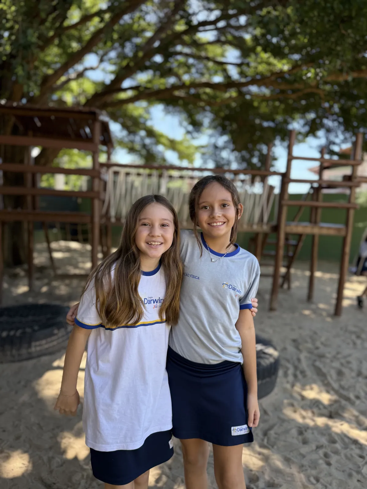 Duas alunas dos Anos Iniciais sorrindo abraçadas no parquinho.