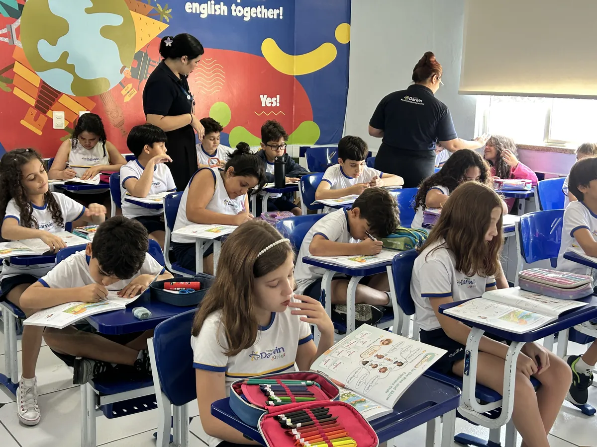 Turma de Anos Iniciais em aula bilíngue com mural 'English Together'.