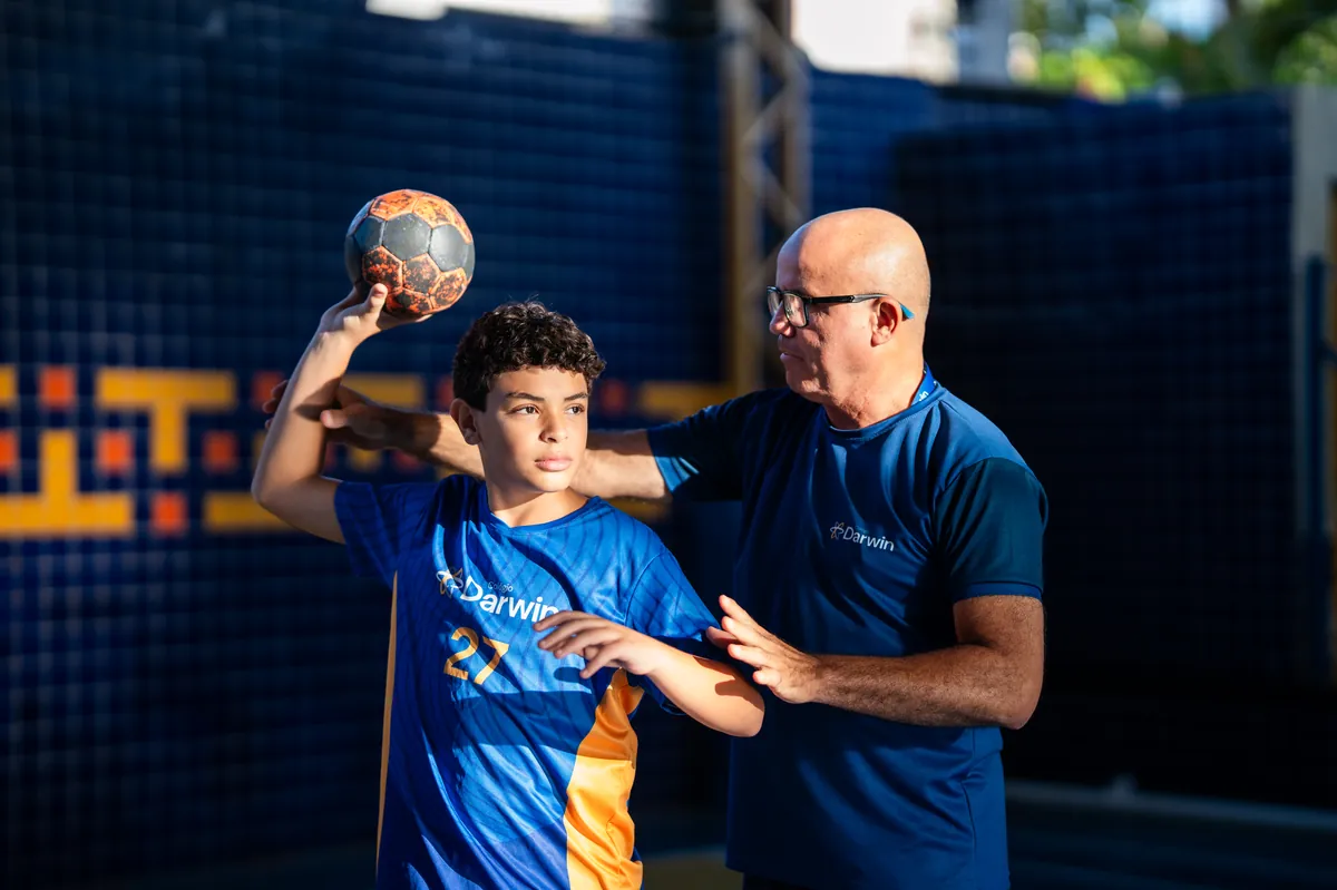 Aluno treinando handebol com o professor no ginásio Darwin