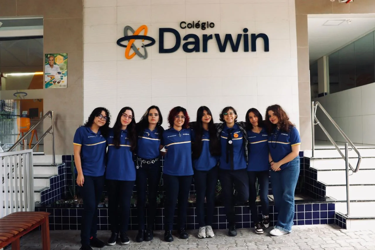 Alunas do Ensino Médio do Darwin reunidas na escada, sob o letreiro do Colégio Darwin.