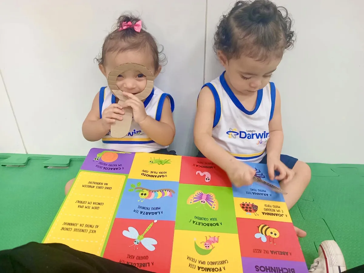 Dois alunos do Infantil deitados no tapete lendo livro juntos.
