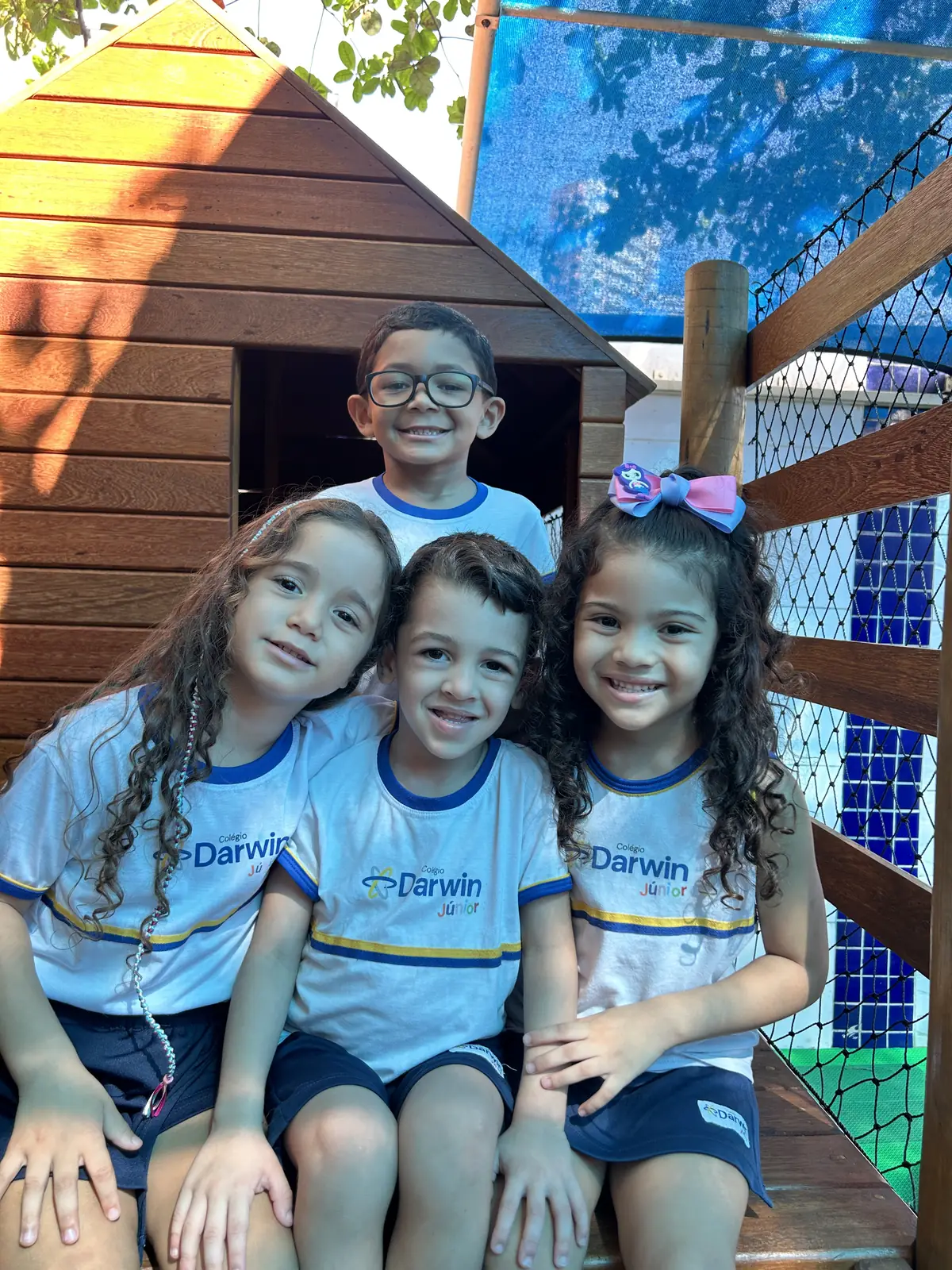 Quatro crianças posando juntas em uma casinha de madeira.