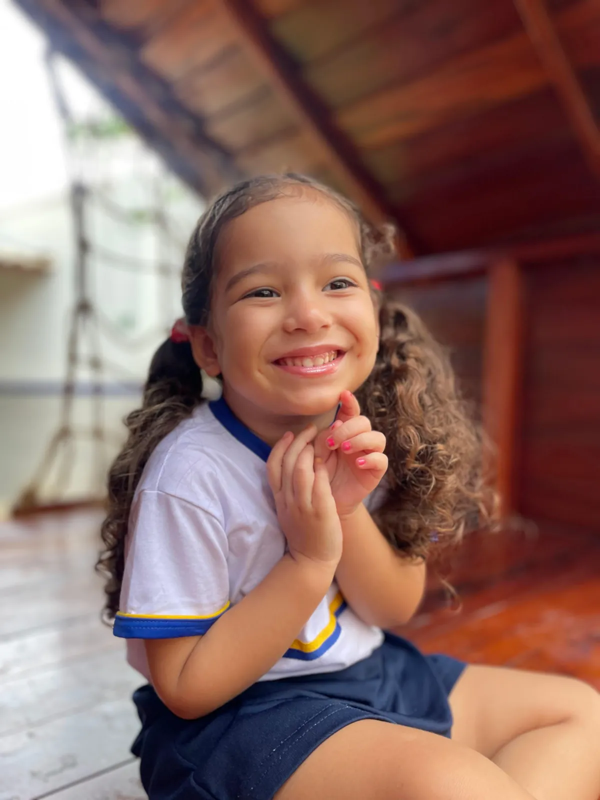 Menina sorrindo dentro de uma estrutura de madeira.