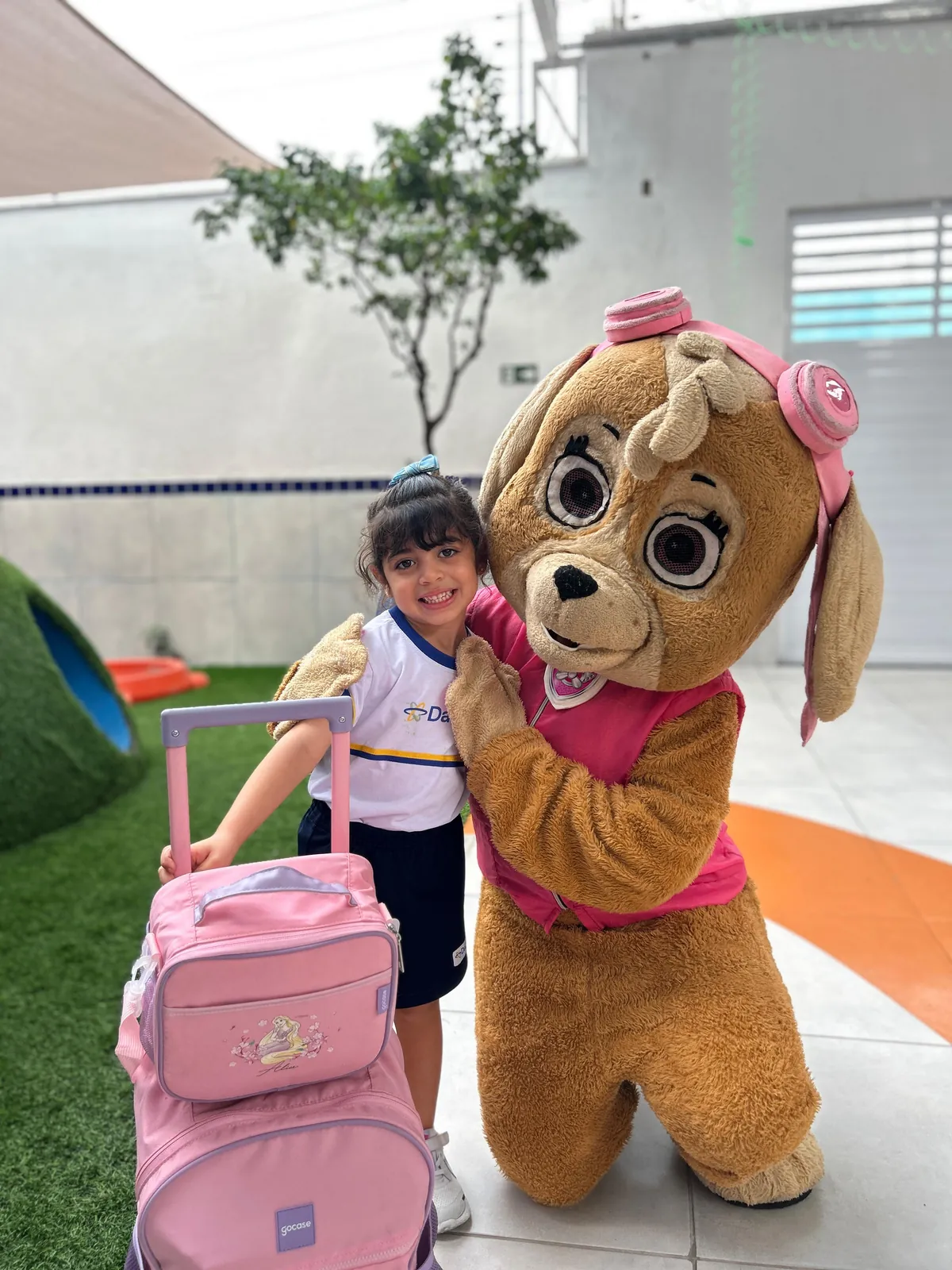 Menina com mochila rosa ao lado de mascote da Patrulha Canina.