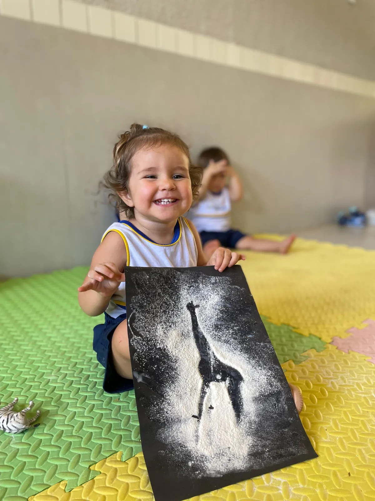 Menina segurando desenho de girafa feito com farinha.