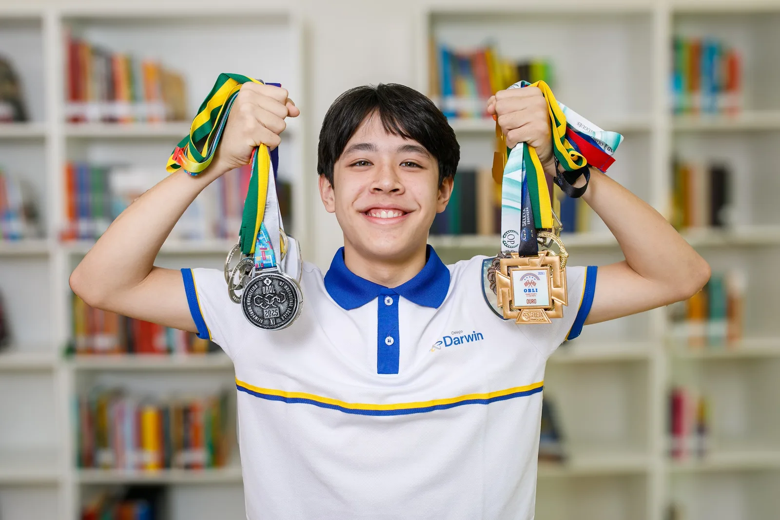 Aluno do Darwin erguendo as medalhas conquistadas em olimpíadas do conhecimento, na biblioteca da escola.