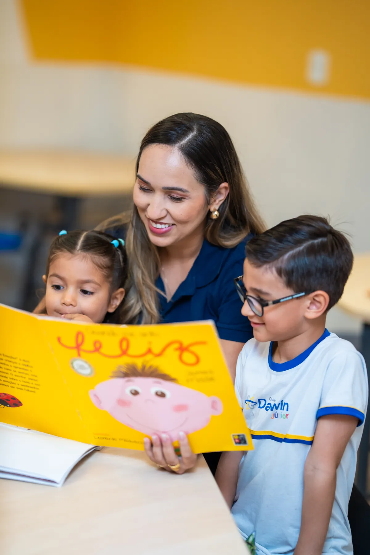 Professora do Darwin lendo com dois alunos da Educação Infantil.