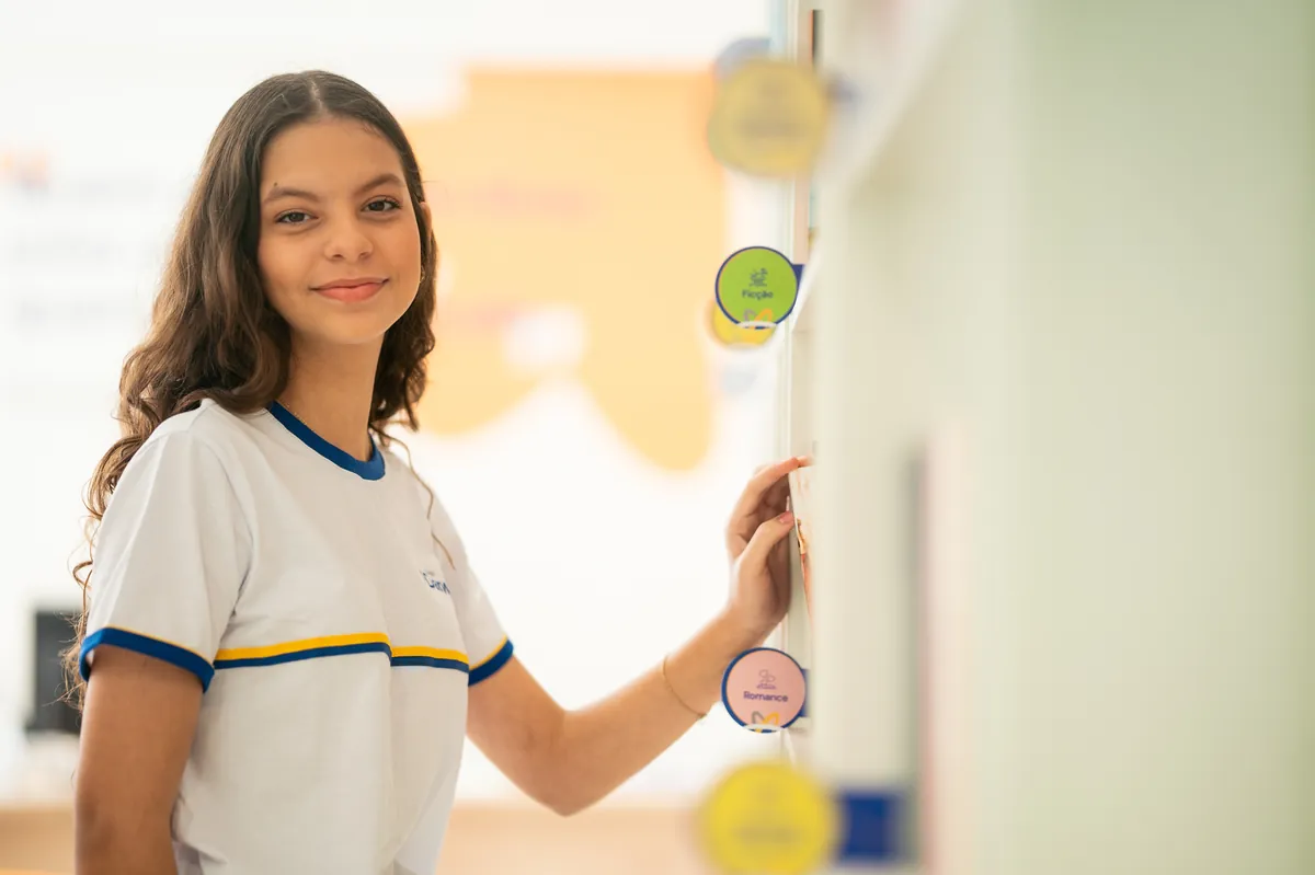 Aluna Darwin sorrindo em frente ao mural de personagens da leitura.