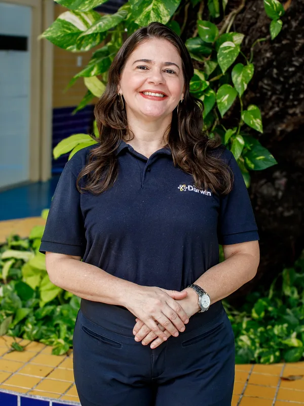 Carol Holanda, supervisora dos Anos Finais do Colégio Darwin, sorrindo diante da árvore do pátio