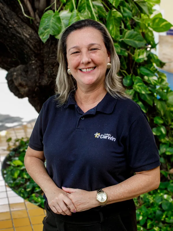 Fernanda Ramos, supervisora da Educação Infantil do Colégio Darwin, sorrindo diante da folhagem do pátio