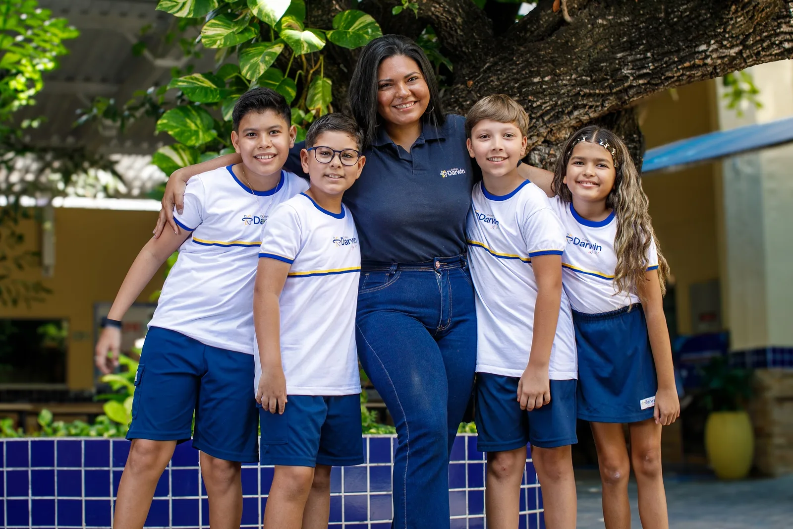 Professora do Colégio Darwin com quatro alunos dos Anos Iniciais sob a árvore do pátio da Sede Aldeota