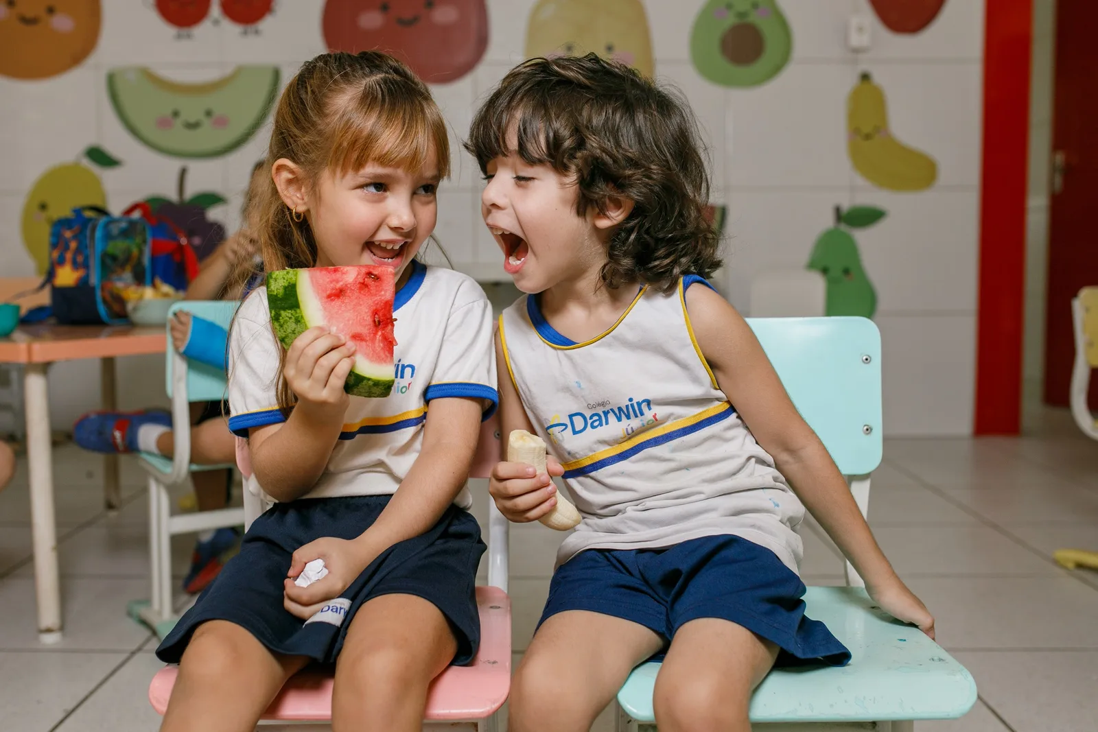 Dois alunos do Darwin sorrindo à mesa do refeitório da sede Sul durante o lanche.